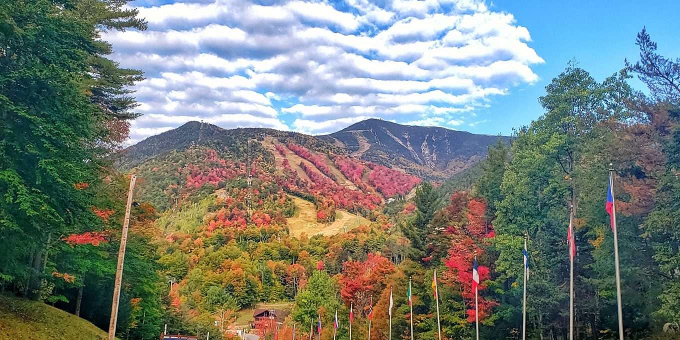 A roadway lined with international flags against an autumnal mountainside