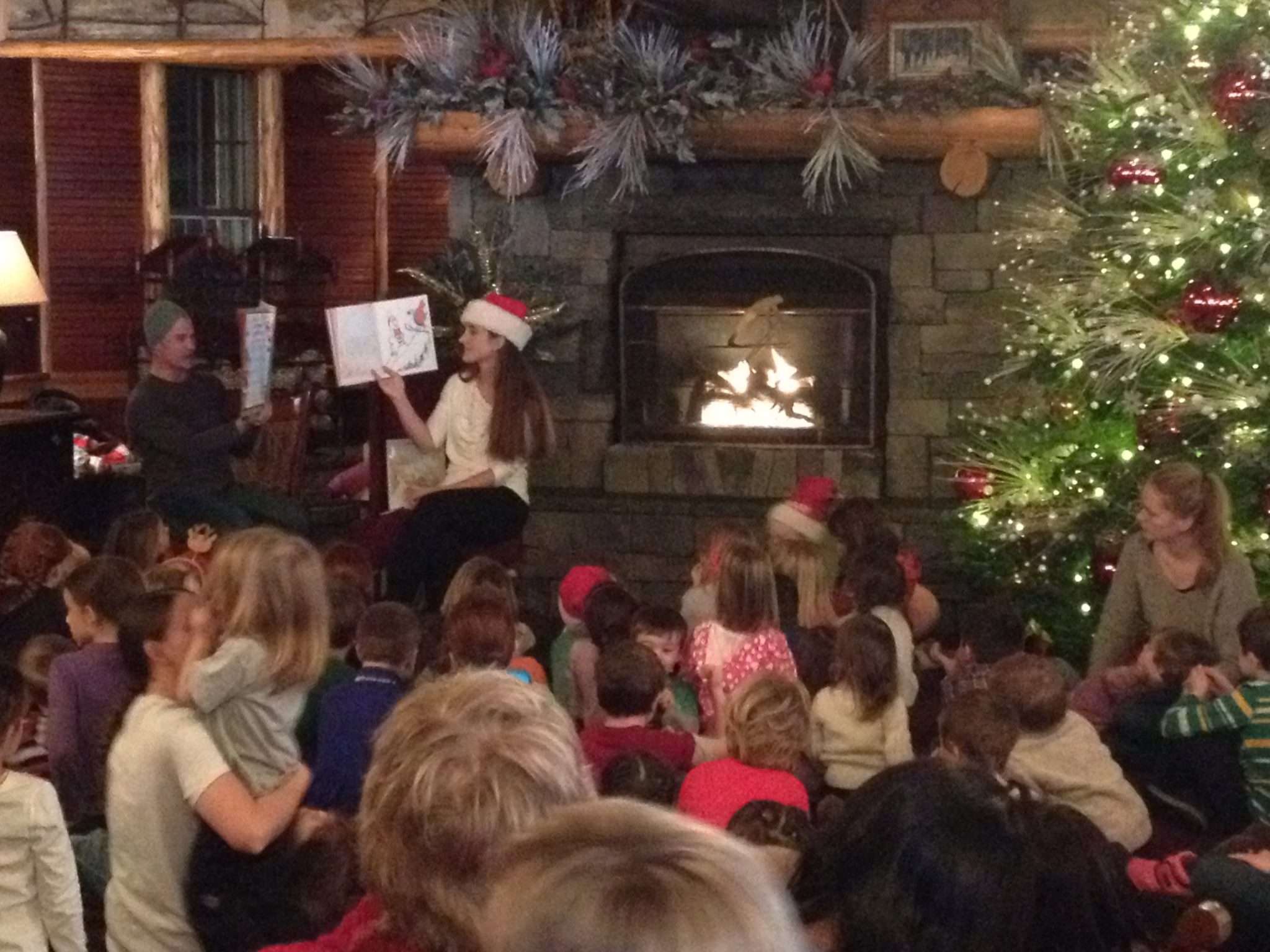 Children gathered around fire with adult reading a christmas story