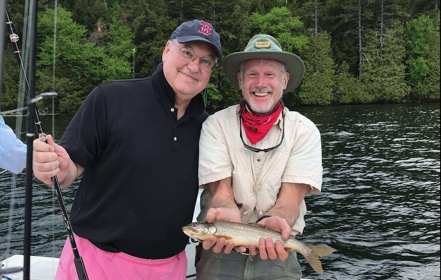 Two men standing on a boat holding a brown trout fish on Lake Placid