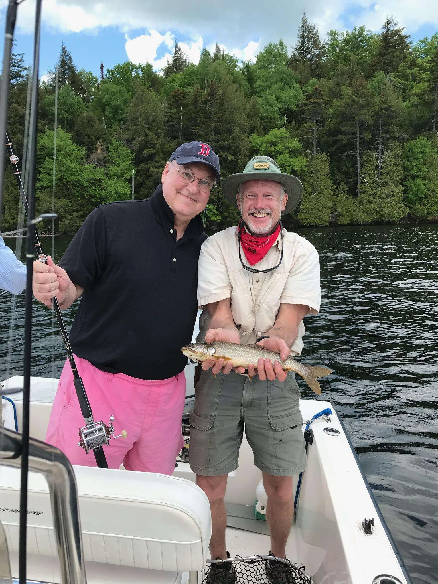 Two men standing on a boat holding a brown trout fish on Lake Placid