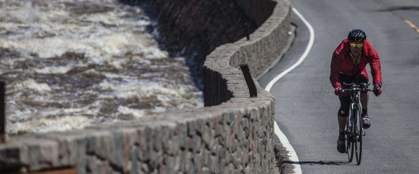 Road biker in a red jacket cycling next to river