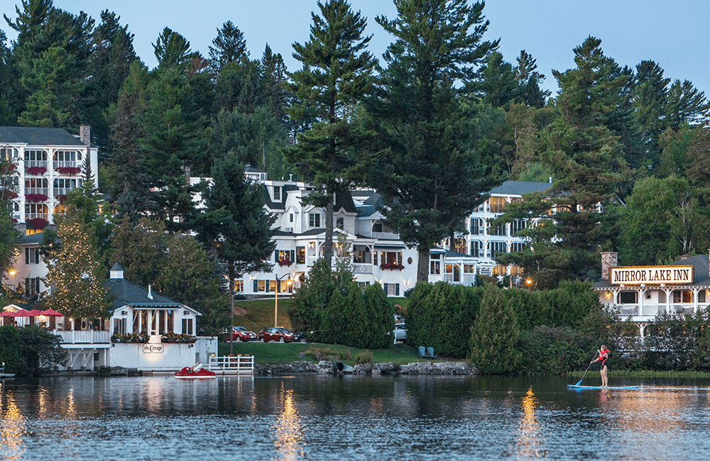 View of Mirror Lake Inn buildings from the lake, with woman paddleboarding