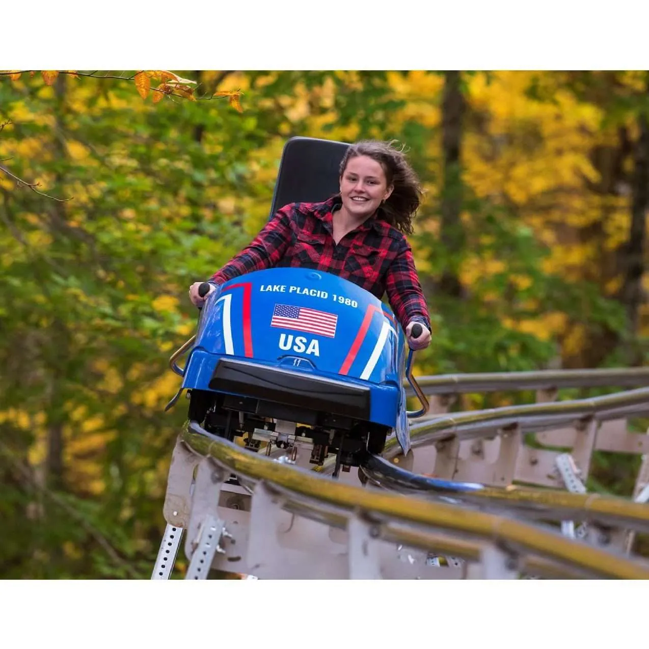 A woman in a red plaid shirt riding a single-person coaster outdoors