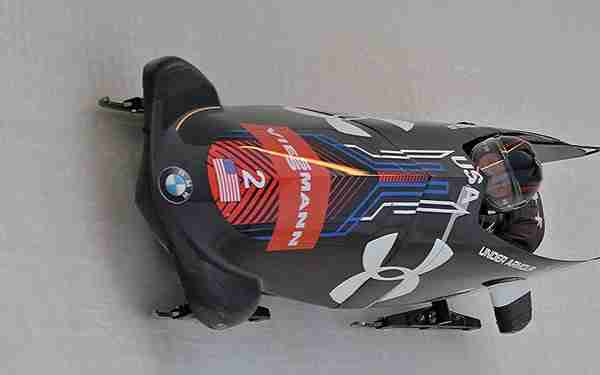 A black bobsled with a single passenger moving down a track