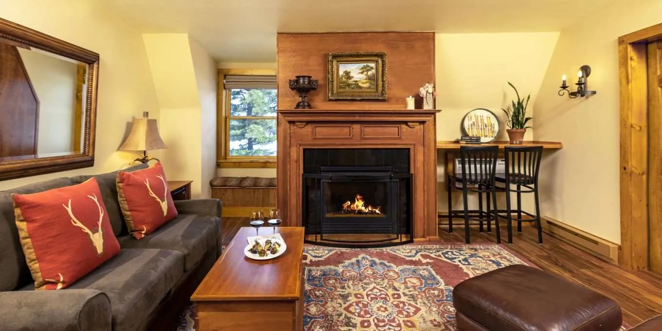 A cozy lit fireplace in the middle of a wall adjacent to a large couch and coffee table