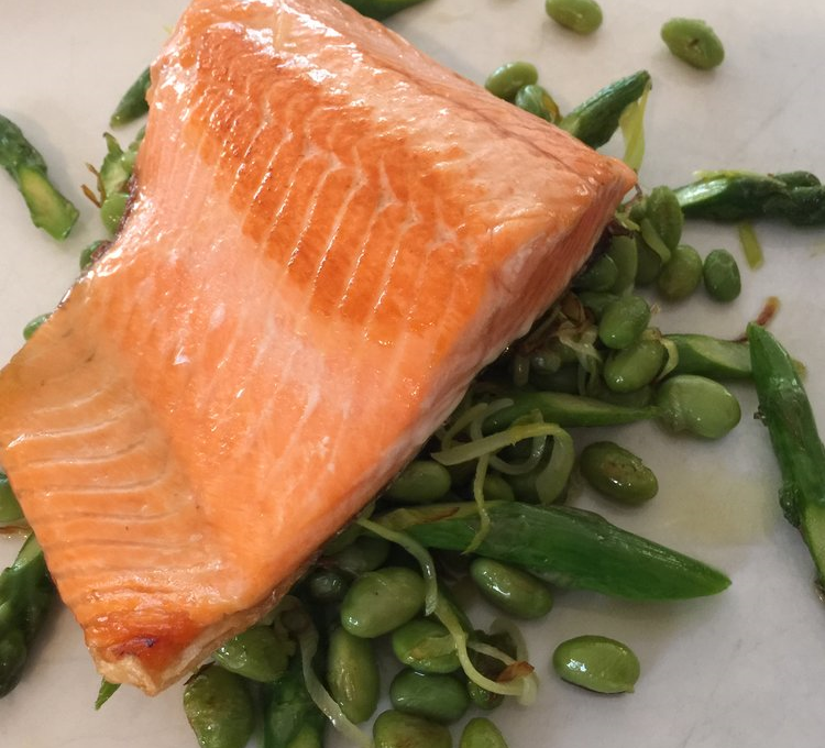 A fillet of salmon on a bed of green beans and peas